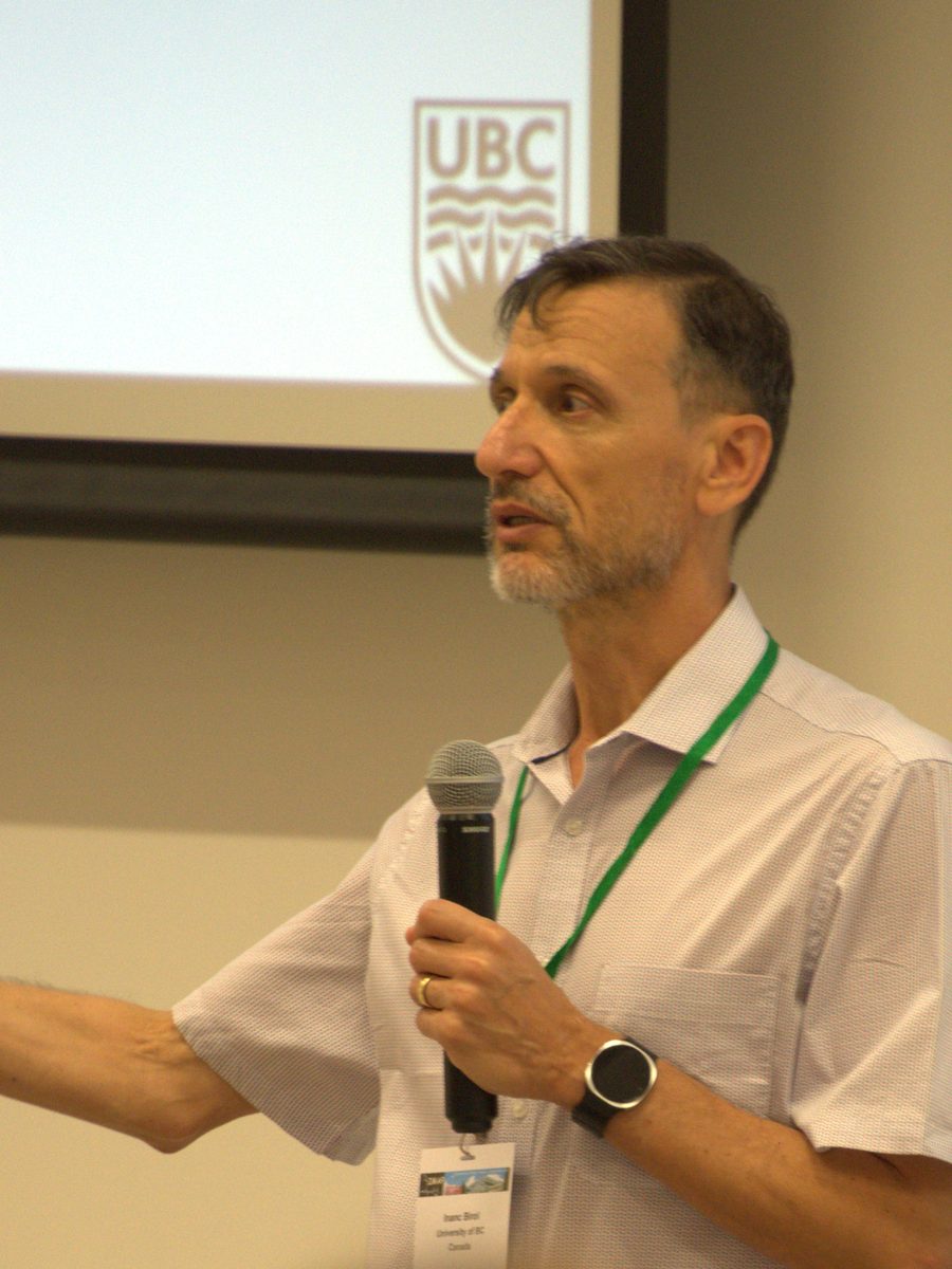 Dr. Inan&ccedil; Birol gesturing mid-talk in front of a University of British Columbia slide