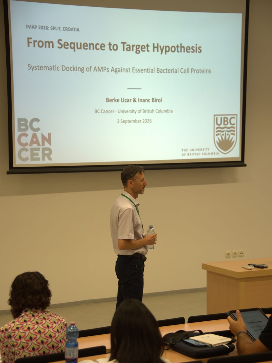 Dr. Inan&ccedil; Birol standing beside his title slide, which reads &ldquo;From Sequence to Target Hypothesis: Systematic Docking of AMPs Against Essential Bacterial Cell Proteins&rdquo;