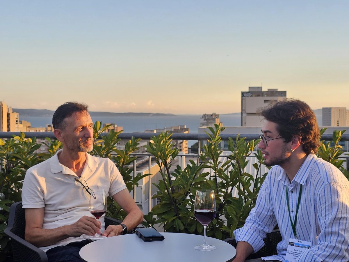 Dr. Inanç Birol and Berke Uçar talking over a drink on a rooftop terrace at sunset, with the Adriatic and the Split skyline behind them